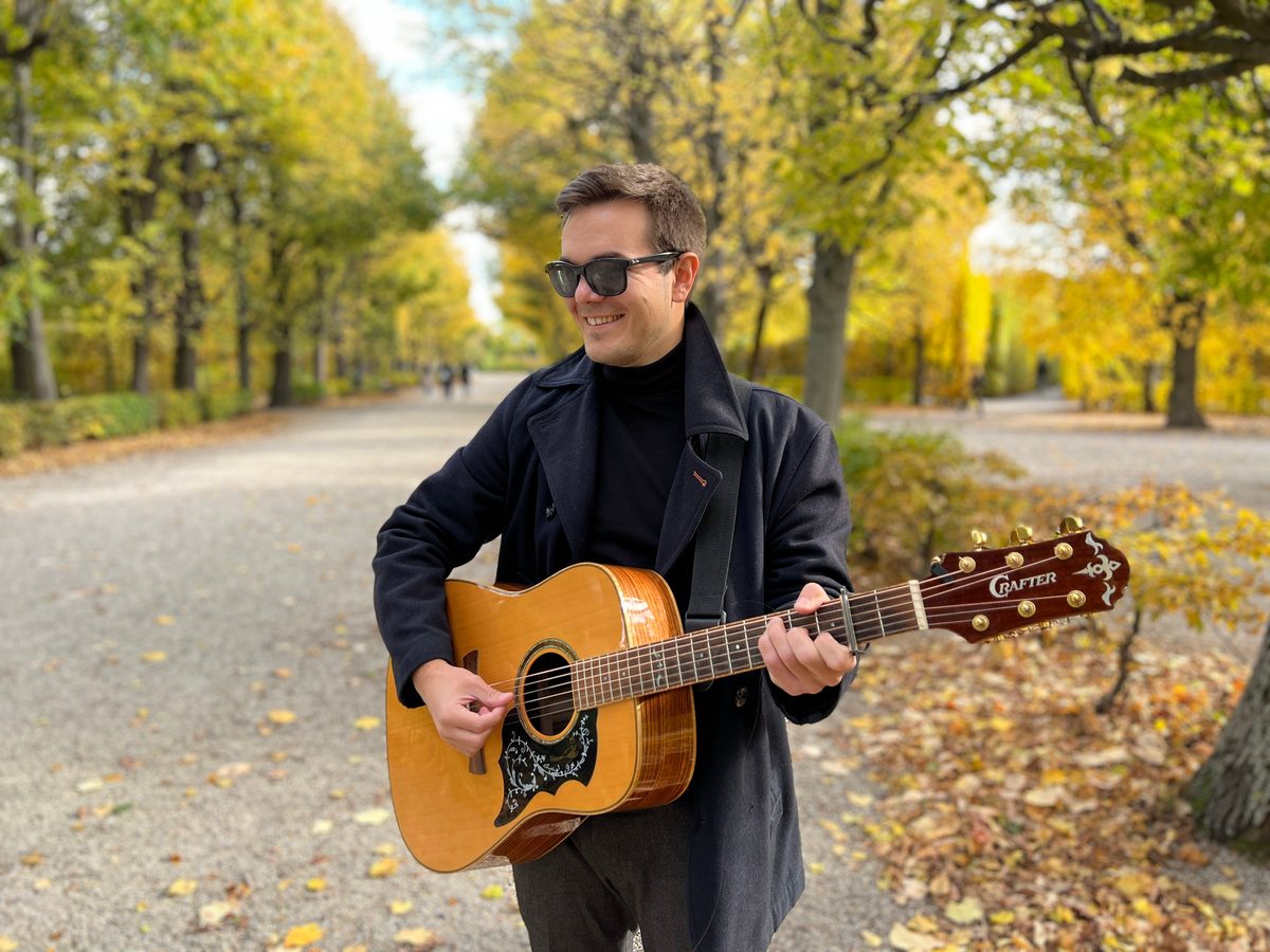 Simon Schütt spielt lächelnd Gitarre in einer Herbstallee